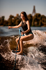 young woman holding rope with and riding down the wave on wakesurf board.
