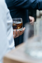 holding a glass of whiskey with ice in his hand