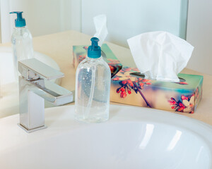 Close up on a sanitizer gel and disposable wipes box on a ceramic sink. Single-use dryer sheets and...