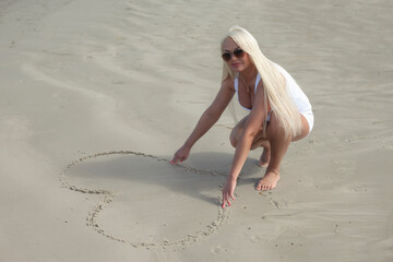 Woman sitting on beach dunes and drawing heart