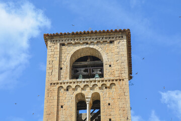 BEGET, CATALONIA, SPAIN, EUROPE, SEPTEMBER 2020. Beautiful tower of the Romanesque church of San Cristóbal surrounded by birds in the beautiful medieval town of Beget.