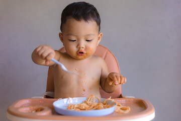 Asian boy eatting on high baby chair.