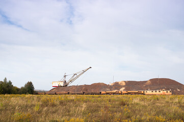A large walking excavator forms dumps of rock delivered by freight train from a mining quarry....