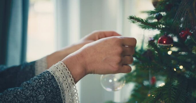Close up on the hands of a young woman decorating a christmas tree at home