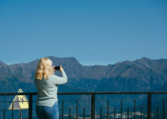 unrecognizable woman with backpack standing on observation deck in mountains blurred background