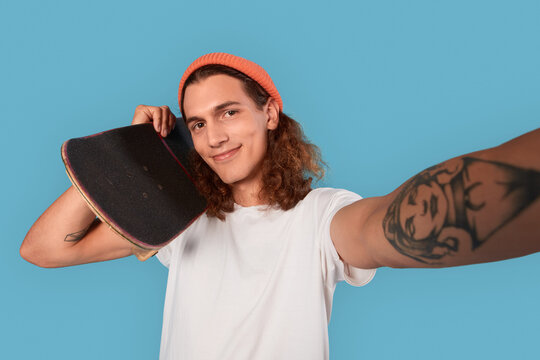 Young adult guy holding skateboard, making selfie