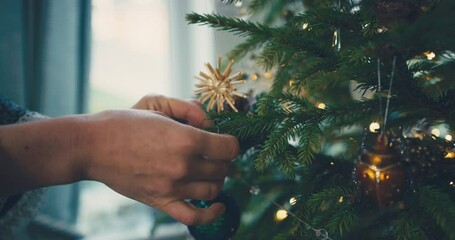 Close up on the hands of a young woman decorating a christmas tree at home