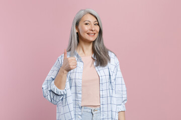 Smiling cheerful beautiful attractive gray-haired asian woman wearing basic white checkered shirt standing showing thumb up looking camera isolated on pastel pink colour background, studio portrait.