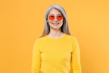 Smiling cheerful beautiful attractive charming pretty gray-haired asian woman wearing casual clothes eyeglasses standing looking camera isolated on bright yellow colour background, studio portrait.
