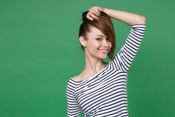 Cheerful smiling funny pretty charming young brunette woman 20s wearing striped casual clothes posing standing holding hair like forelock looking camera isolated on green background, studio portrait.