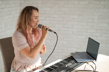 A woman sings into a microphone and shoots a video blog on a laptop