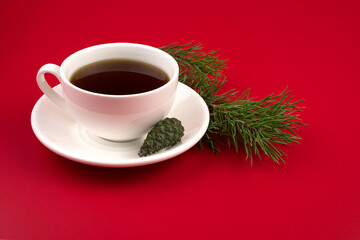 A Cup of coffee on a white saucer, pine branches and cones on a red background. The concept of the new year 2021 and Christmas.