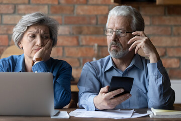 Confused mature man and woman calculate household finances expenditures, have debt problem paying...