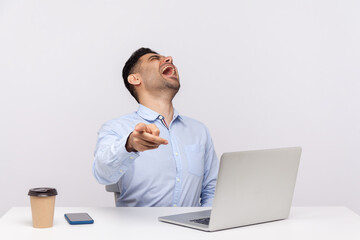 Amused delighted businessman sitting office workplace with laptop on desk, pointing finger to camera and laughing out loud, noticing teasing ridiculous coworker. indoor studio shot isolated on white