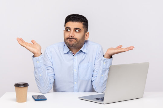 Don't know! Puzzled clueless confused businessman sitting office workplace with laptop on desk, shrugging shoulders, doubting can`t make decision. indoor studio shot isolated on white background