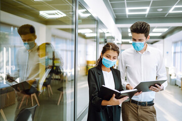 Business colleagues wearing medical face mask discussing together work issues at office. Teamwork during pandemic in quarantine city. Covid-19.