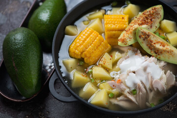 Close-up of ajiaco or colombian potato, chicken and corn stew topped with avocado slices and sour cream, selective focus