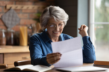 Excited senior Caucasian grey-haired woman triumph reading good news in postal paper letter at...