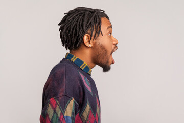 Side view extremely excited surprised african man with dreadlocks looking ahead with big eyes and open mouth, wondered, amazed with news. Indoor studio shot isolated on gray background