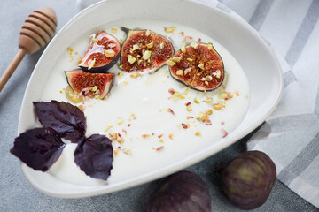 Bowl of greek yogurt with sliced fig fruits, honey, red basil and chopped nuts, close-up, horizontal shot
