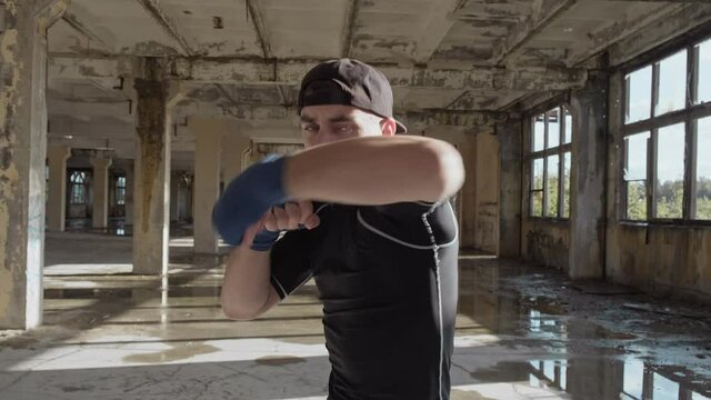Boxer punching to camera. Young boxer practicing boxing punches looking at camera in abandoned factory. Slow motion. Close-up in 4K, UHD
