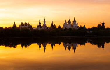Fototapeta na wymiar Awe orange sunset over blurry reflection of the Izmailovsky Kremlin in the lake water at Moscow, Russia. Russian landscape in warm colors