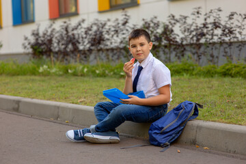 schoolboy in a white shirt with a blue tie, holds a blue lunch box and a slice of apple, looks at the camera