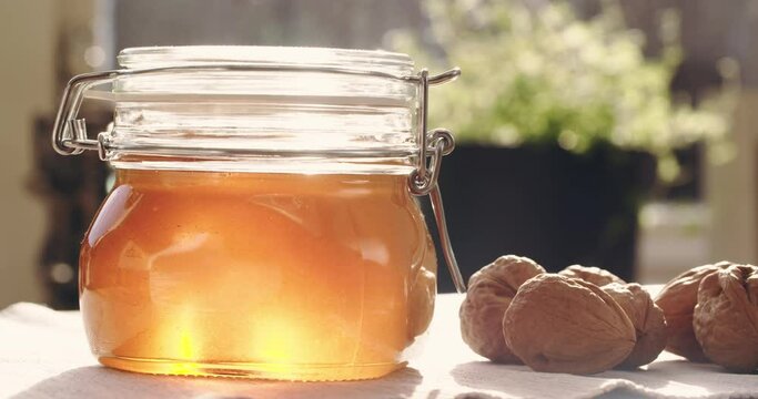 Eye level shot of liquid honey in a glass jar next to whole walnuts.
