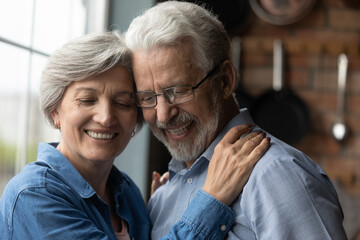 Happy elderly Caucasian man and woman embrace satisfied with good healthy calm joyful retirement together. Smiling mature 60s grey-haired couple husband and wife hug show love and care in relations.