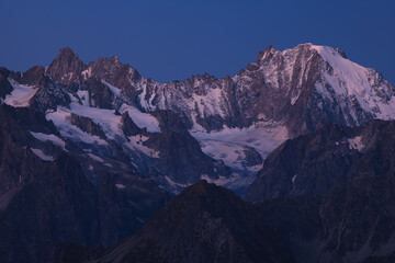 View on purple ridge of Mont Blanc massif with gentle snow and dark rocks during blue hour in clear dark blue sky