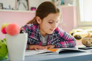 Cute little school girl studying at home in her room. Girl doing homework at home.