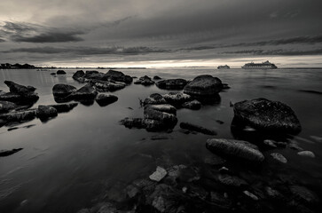 Fototapeta na wymiar Finnish gulf at sunset with stones and 2 passenger ships in black and white