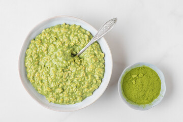 oatmeal porridge with matcha powder in a bowl with a spoon for healthy diet breakfast on white background. top view