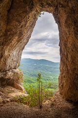 Amazing view through the hole in the rock  with red rocks on the walls around on the distant mountains and forests during early spring
