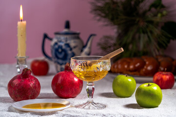 Apples, pomegranates, honey and wicker challah on a wooden table.