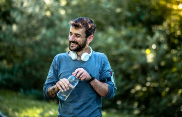 The young man pauses during training, rests, closes the bottle of water and smiles
