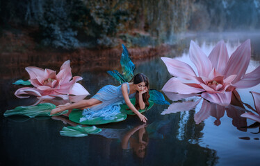 Panele Szklane  Piękna kobieta, mała urocza wróżka ze skrzydłami motyla, leży na zielonym liściu lilii wodnej. Fantasy dekoracje ogromne różowe kwiaty na jeziorze. Nimfa rzeczna, dziewczyna pixie w niebieskiej sukience dziewczyna dotykająca wody