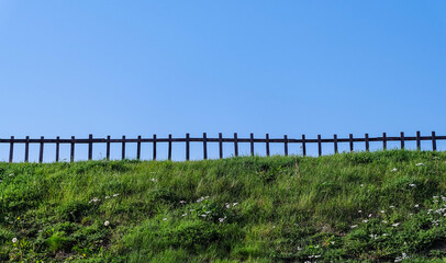 Fototapeta na wymiar A low wooden fence standing on the lawn against the blue sky