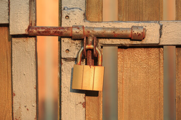 Rusty metal padlock and bolt locking the old wooden gate
