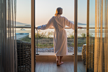 Beautiful woman from back in bathrobe on terrace of hotel room with Sea View