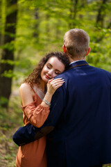 Beautiful couple in the woods. Girl with elegant haircut hugs her man in a suit. Rustic outdoors details photography portrait. Happy woman and boyfriend