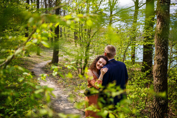 Naklejka na ściany i meble Romantic walk of a young couple in a green forest, warm spring weather. Guy and girl hugging in nature