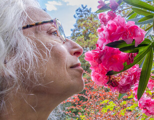 Begegnung einer älteren, grauhaarigen Frau im Profil mit dem Gesicht einer pinken Oleanderblüte