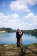 Happy and young newlyweds go holding hands and laughing, on the background of a lake and a green meadow. Groom and beautiful bride with curly hair are walking in the meadow. Joyful summer day