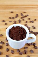 Cup of Ground Coffee on Wooden Table with Scattered Roasted Coffee Beans