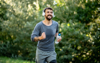A young man jogs in nature on a treadmill and listens to music on a sunny day