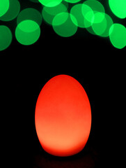Shining Vibrant Red Egg Shaped Table Lamp with Vivid Green Bokeh Light on Dark Background