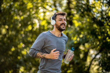 A young man jogs in nature, listens to music and carries a bottle of water with him