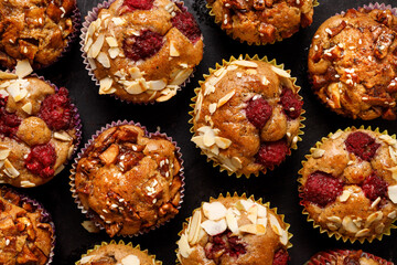 Homemade muffins with raspberries and nuts on a black background top view