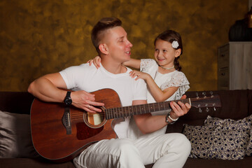 Pretty young man father with four-year-old girl daughter with guitar in interior of room. Happy family with guitar. Concept of home learning or playing guitar at home. Copyright space for site